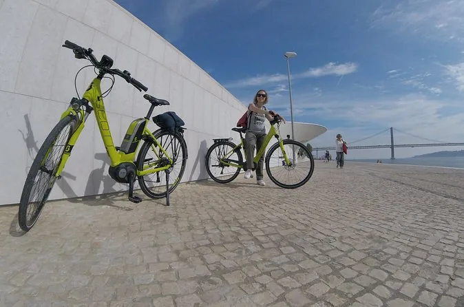 Electric bikes by the curved white MAAT building on the river