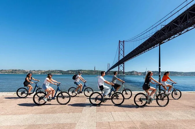 Cyclists riding along the river beneath the 25 de Abril Bridge